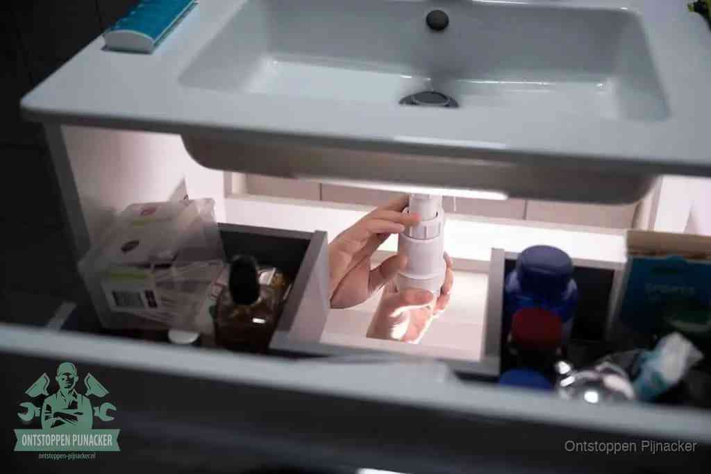 Een pompfles met zeep boven een wastafel, de heet water en afwasmiddel-methode om een vetprop in de afvoer los te maken in Pijnacker