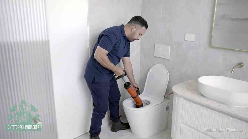 Een monteur buigt over een wandcloset en duwt met de hand een persluchtontstopper in de toiletpot om de verstopping handmatig los te maken in Pijnacker