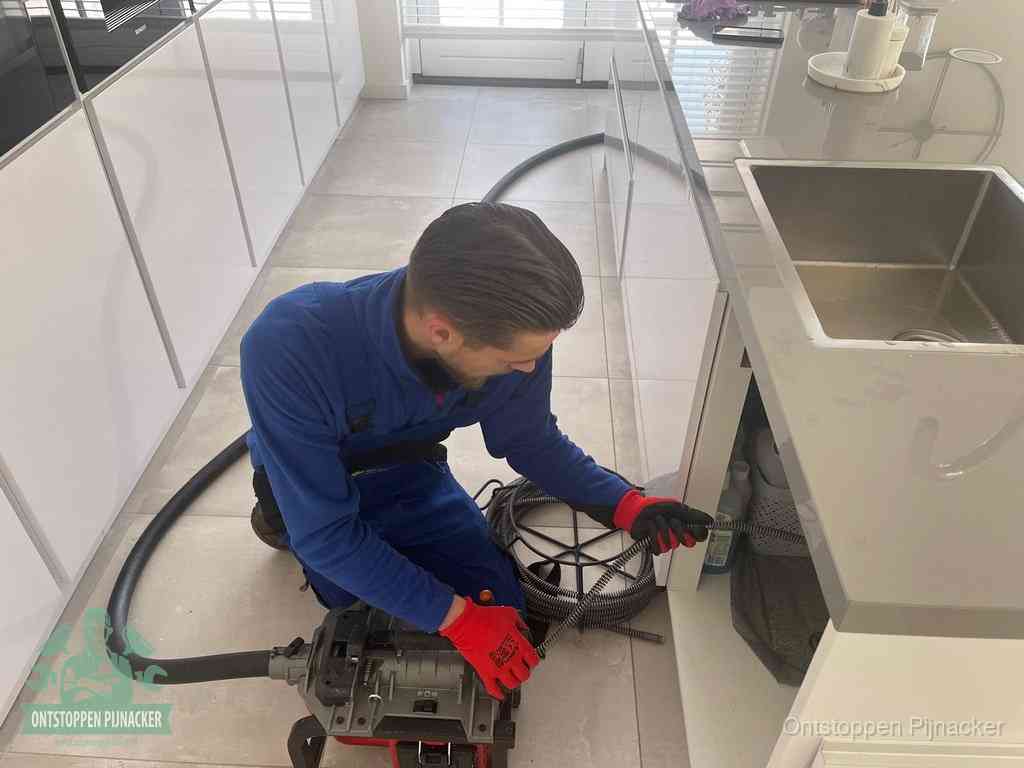 Een monteur ontstopt de keukenafvoer onder de spoelbak met een elektrische veermachine in Pijnacker