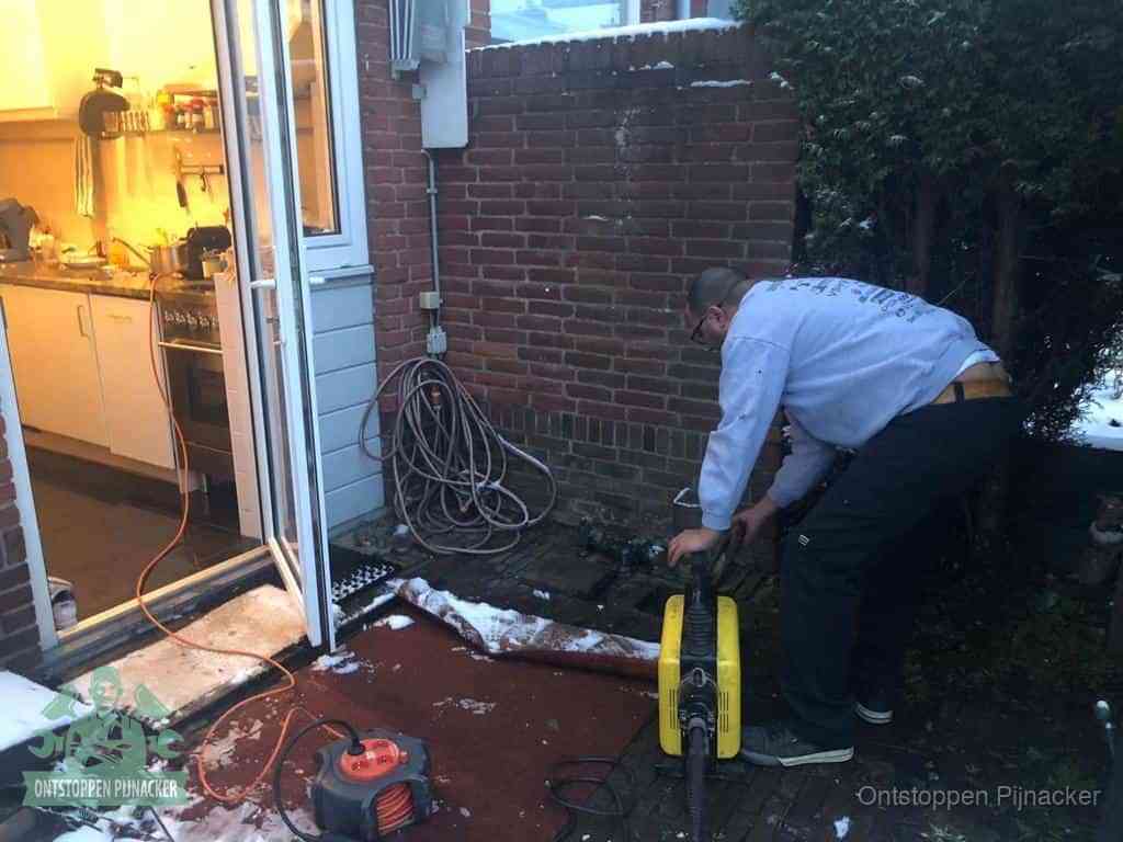 Een monteur werkt buiten bij een open riool-/grondput met een elektrische ontstoppingsmachine om een verborgen afvoerprobleem op te sporen in Pijnacker