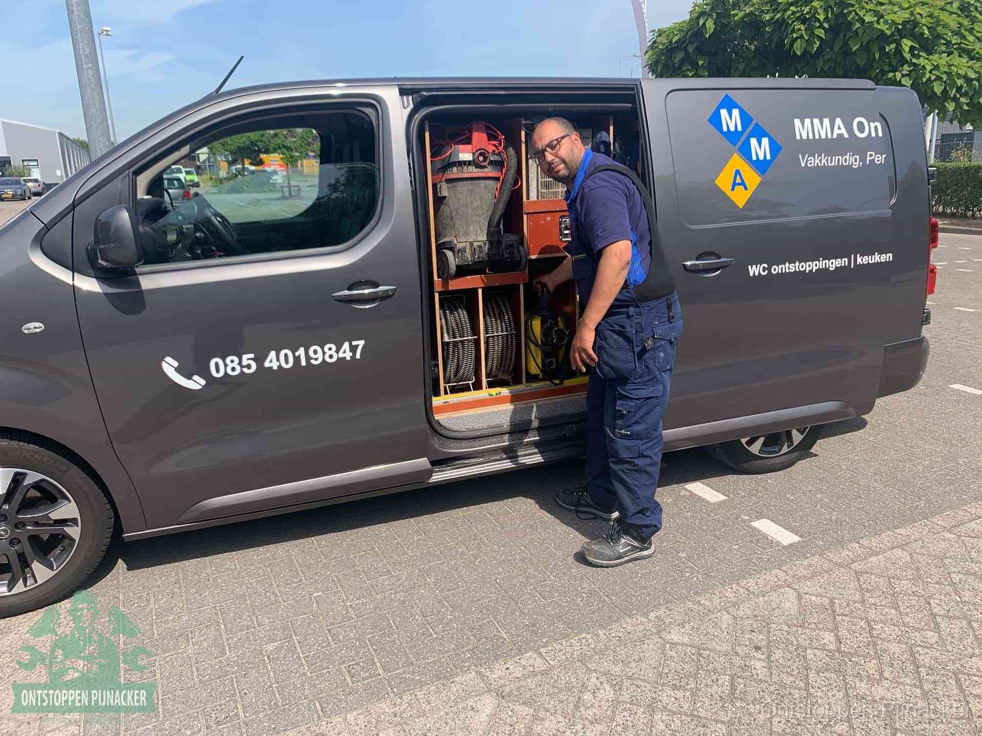 Een monteur bij de open schuifdeur van zijn bedrijfsbus op een parkeerplaats, klaar om de oorzaak van terugkerende afvoerverstoppingen aan te pakken in Pijnacker