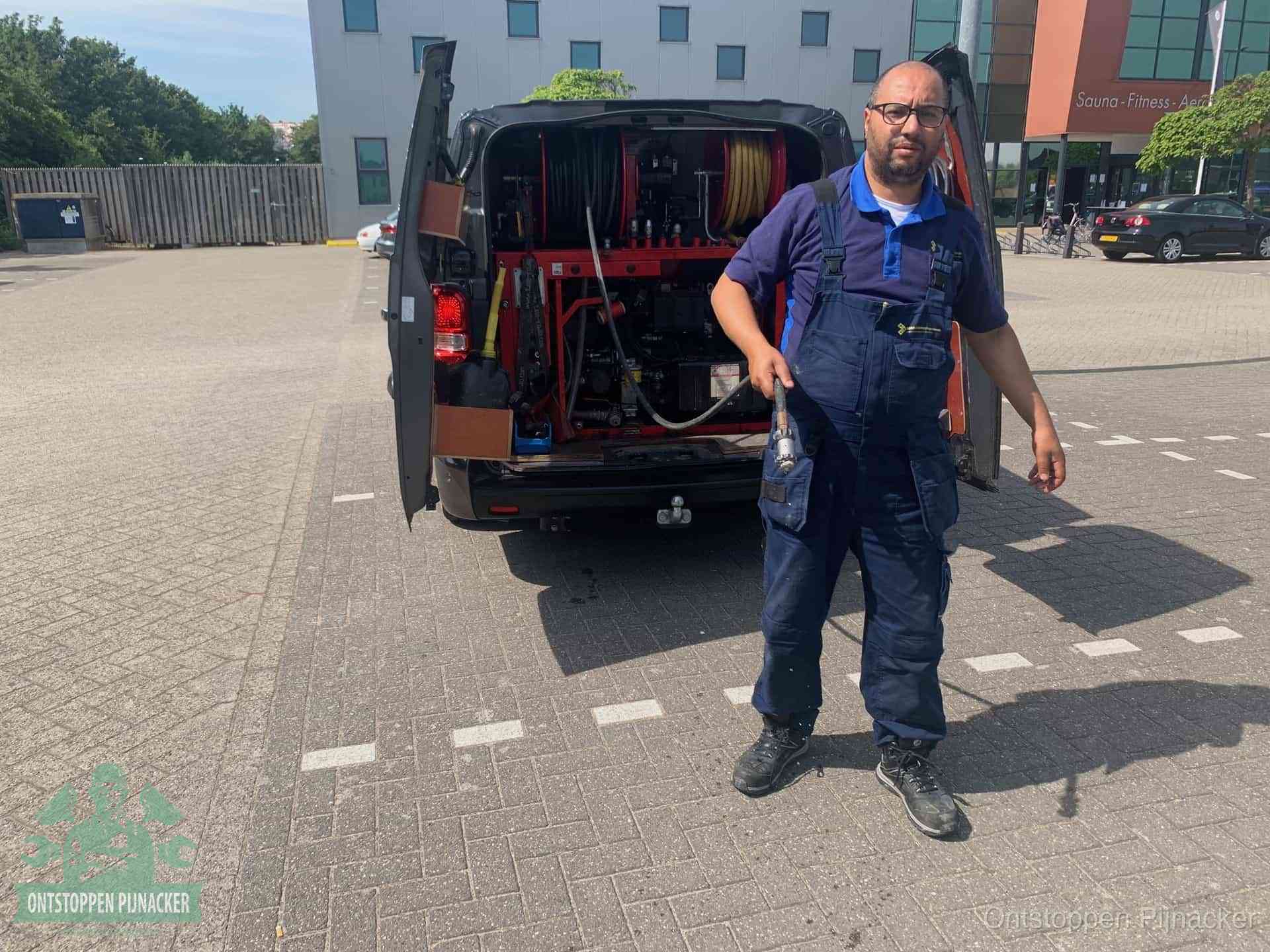 Een monteur bij zijn bestelbus met een hogedruk- en rioolreinigingsunit, klaar om de oorzaak van terugkerende wc-verstoppingen aan te pakken in Pijnacker