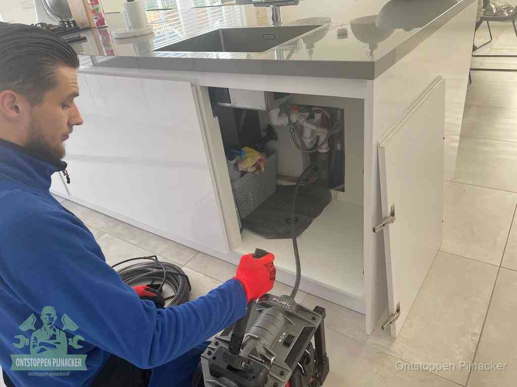 Monteur ontstopt met een veermachine een verstopte afvoer onder de gootsteen in Pijnacker