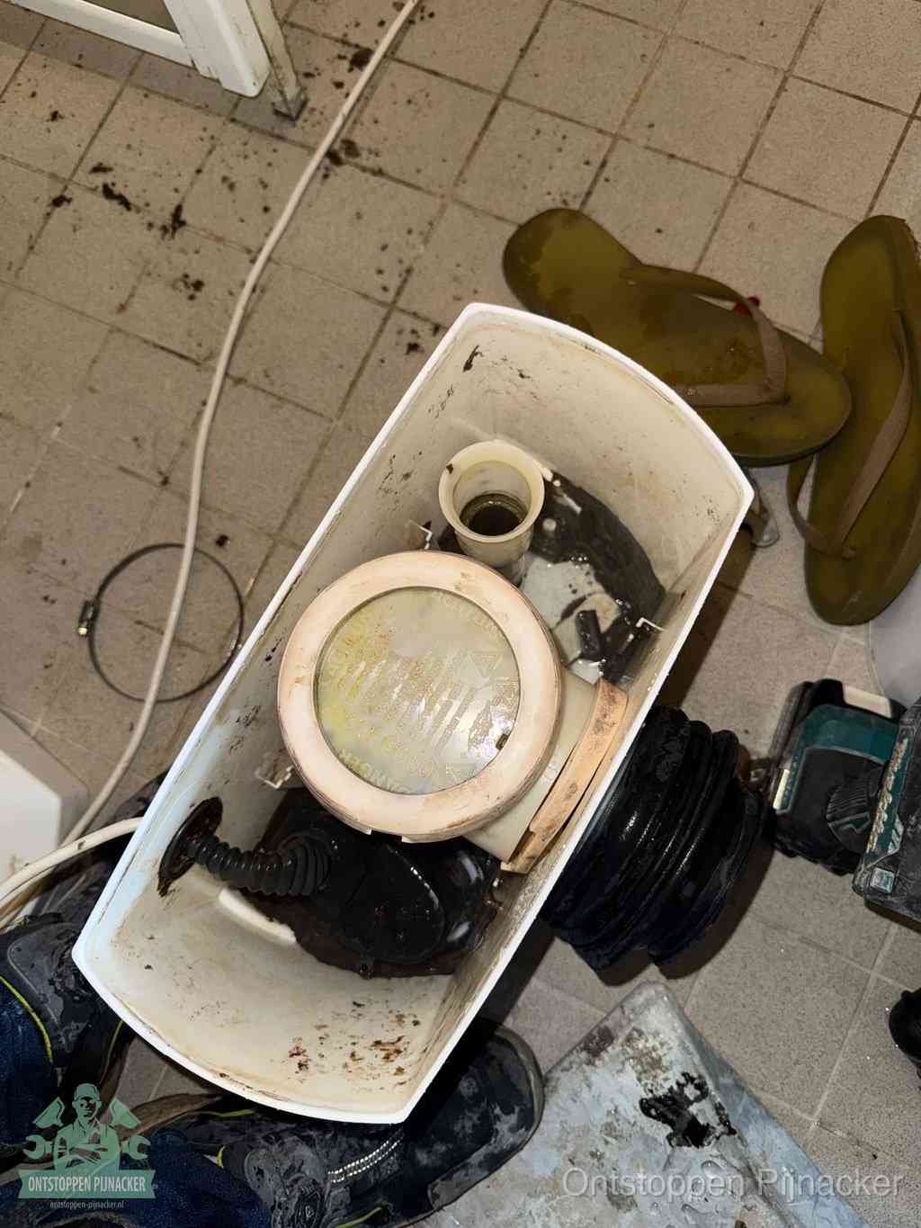 Een gedemonteerde toiletpot op de vloer met ontstoppingsveer en gereedschap ernaast, het verwijderen van een vastzittend voorwerp uit de wc in Pijnacker