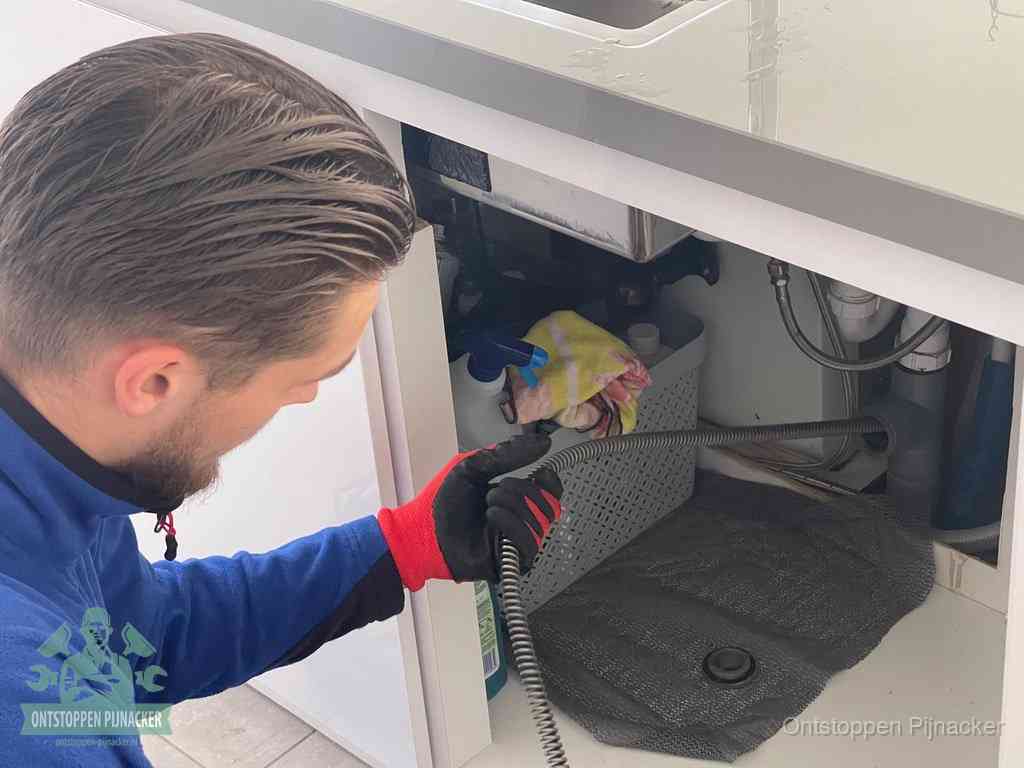 Een monteur voert een flexibele ontstoppingsveer in de afvoer om een verstopping voorbij de bocht van het toilet te bereiken in Pijnacker