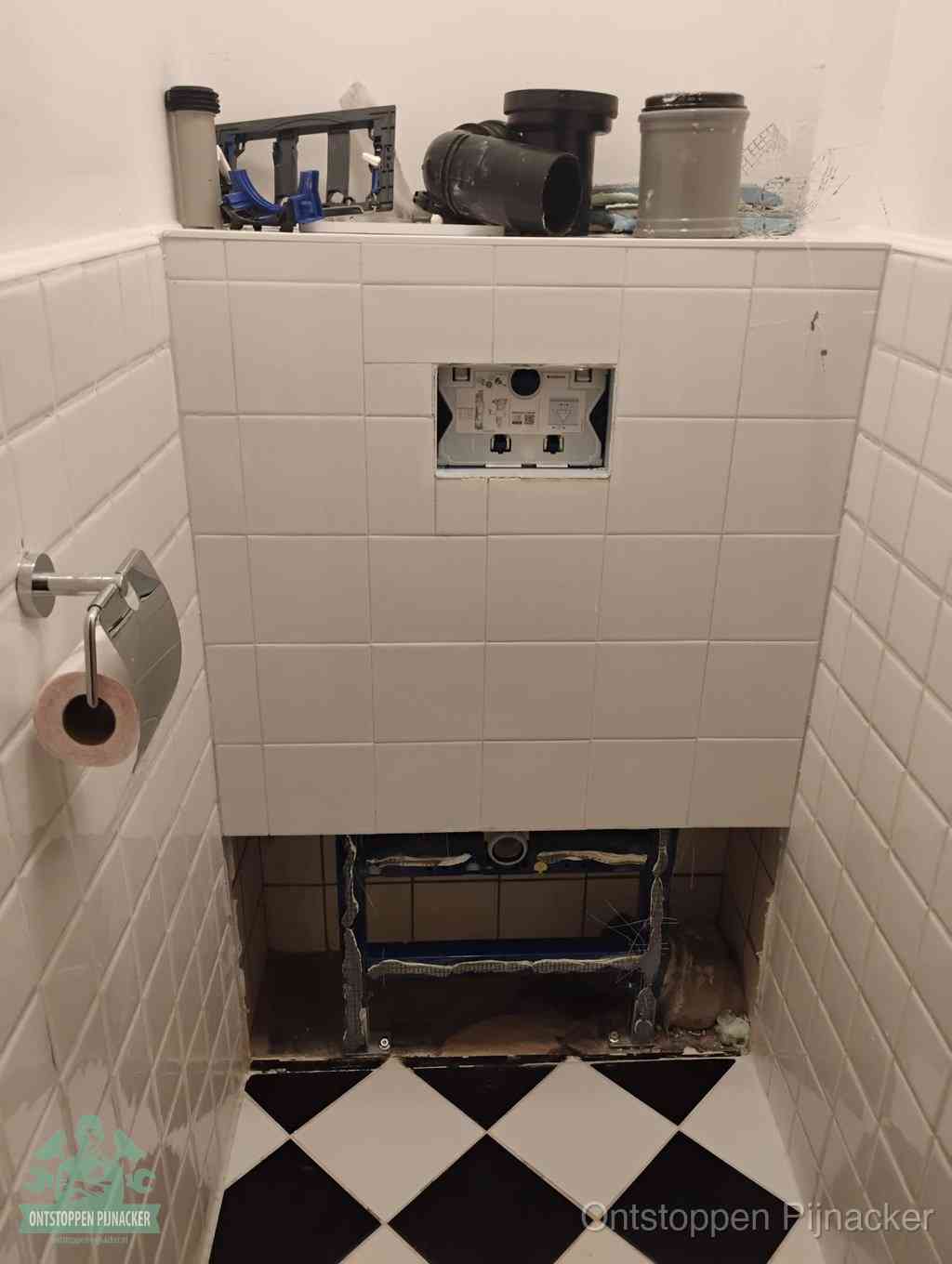 Een toiletruimte waar het hangtoilet en de inbouwreservoir-onderdelen zijn vrijgelegd voor onderhoud, periodiek nazicht voorkomt een wc-verstopping in Pijnacker