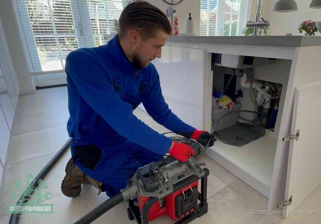 Een monteur voert een professionele elektrische ontstoppingsmachine in de afvoer onder de spoelbak tijdens het gootsteen ontstoppen in Pijnacker